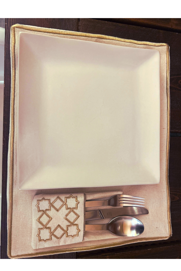 The Arabesque Table Set - 15 Piece Bronze Embroidered set from Raw Cotton placed in a handmade basket with leather handles. This picture shows the placemat & cutlery holder.