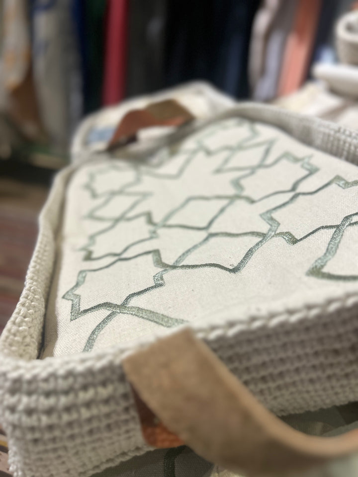 The Arabesque Table Set - 15 Piece Sage Embroidered set from Raw Cotton placed in a handmade basket with leather handles. This picture shows the handmade basket that the set comes in with the leather handles.