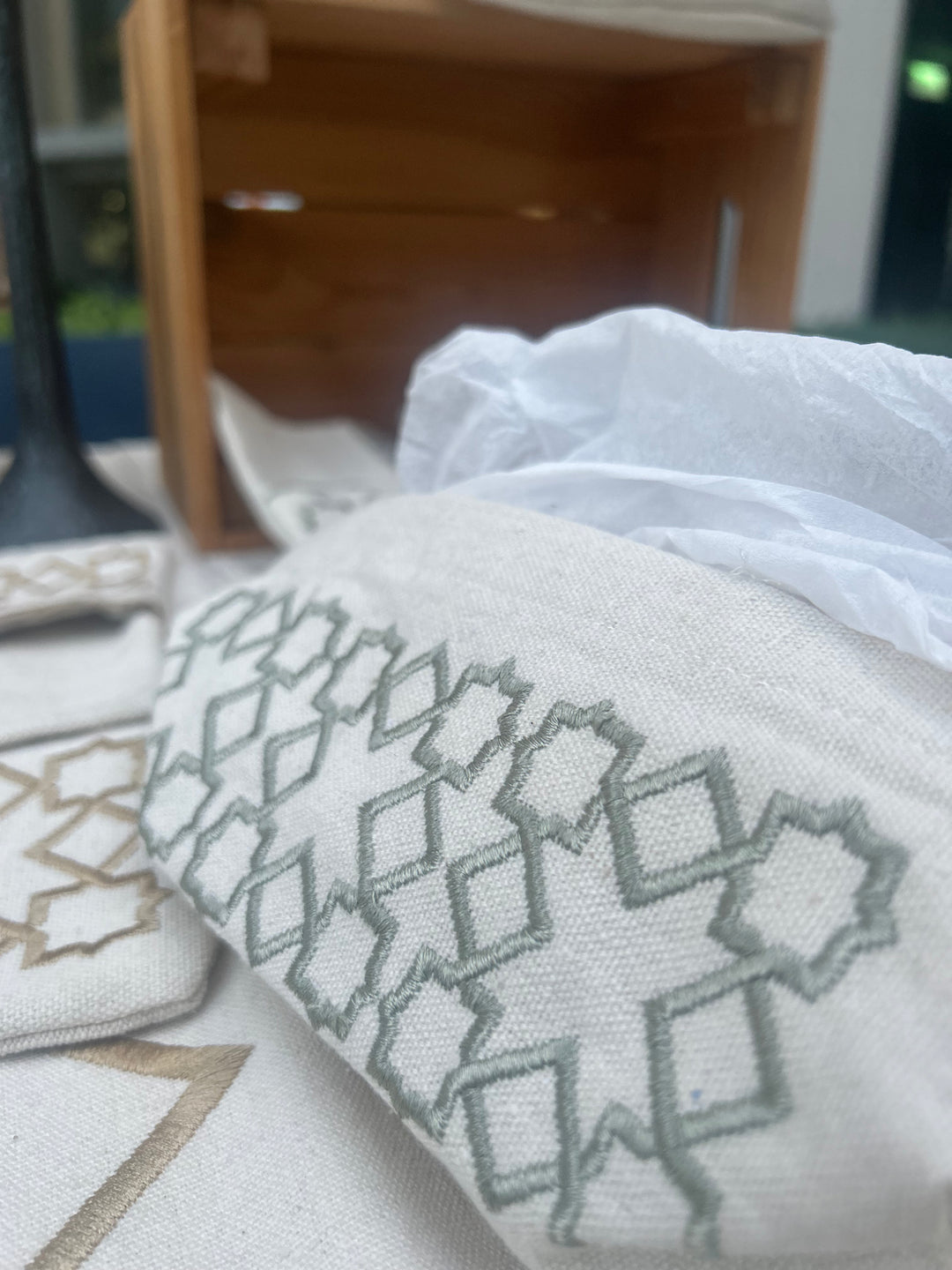 The Arabesque Table Set - 15 Piece Sage Embroidered set from Raw Cotton placed in a handmade basket with leather handles. This picture shows the tissue box cover.