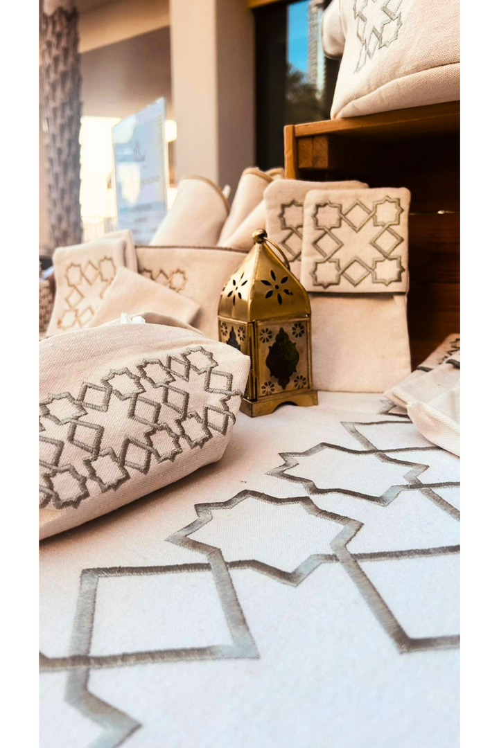 The Arabesque Table Set - 15 Piece Sage Embroidered set from Raw Cotton placed in a handmade basket with leather handles. 